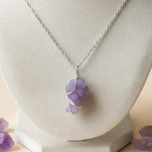 Peut inclure: Un collier à chaîne argentée avec un pendentif composé de petites perles violet clair. Les perles sont enfilées sur du fil de fer et suspendues à une chaîne délicate. Des cristaux d'améthyste sont disposés à la base.