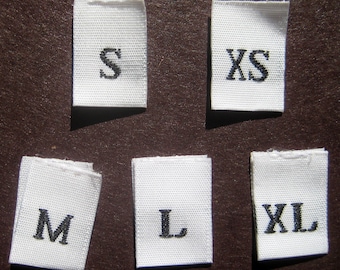 Może przedstawiać: Sześć białych etykiet tekstylnych z czarnym nadrukiem oznaczającym różne rozmiary: XS, S, M, L, XL.