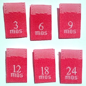 May include: Six pink fabric labels with white text indicating different sizes in months. The labels read 3 mos, 6 mos, 9 mos, 12 mos, 18 mos, and 24 mos.