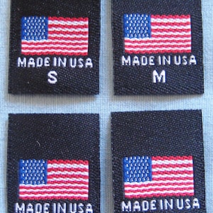 May include: Four black fabric labels with white text and a small American flag. The labels are for sizes S, M, L, and XL. Each label reads "Made in USA".