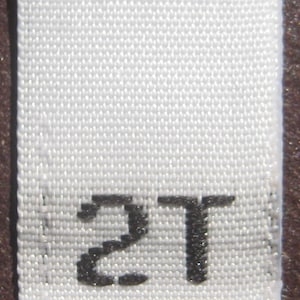 May include: White woven clothing label with the number "2T" printed in black.