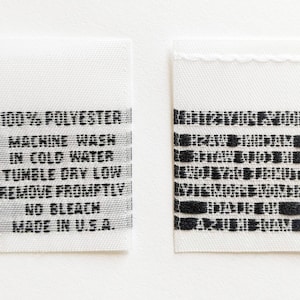 May include: White fabric care label with black text. The label reads: "100% Polyester, Machine Wash in Cold Water, Tumble Dry Low, Remove Promptly, No Bleach, Made in U.S.A."