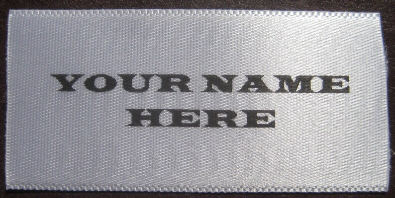Puede incluir: Una etiqueta de sat&eacute;n blanco con texto negro que dice "YOUR NAME HERE".