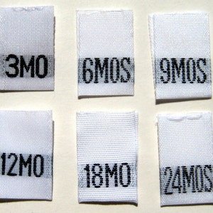 Könnte beinhalten: Sechs weiße Stoff-Etiketten mit schwarzem Text, die verschiedene Größen in Monaten angeben: 3 Monate, 6 Monate, 9 Monate, 12 Monate, 18 Monate und 24 Monate.