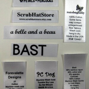May include: A collection of white satin labels with black text. The labels include the names of different businesses, such as "Forevalette Designs", "PC Dog", and "ScrubHatStore". Some labels include care instructions, such as "Machine Wash Cold" and "Tumble Dry Low".
