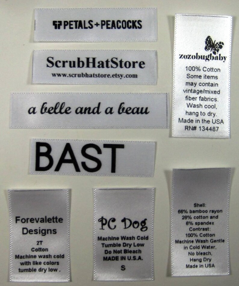 May include: A collection of white satin labels with black text. The labels include the names of different businesses, such as "Forevalette Designs", "PC Dog", and "ScrubHatStore". Some labels include care instructions, such as "Machine Wash Cold" and "Tumble Dry Low".