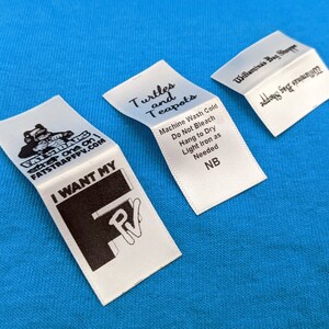 May include: Three white fabric labels with black text. The first label has a cartoon turtle and the text "Turtles and Teapots". The second label has the text "Machine Wash Cold, Do Not Bleach, Hang to Dry, Light Iron as Needed, NB". The third label has the text "Willamina's Bag Shoppe, address for inquiries".