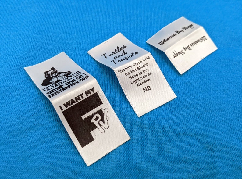 May include: Three white fabric labels with black text. The first label has a cartoon turtle and the text "Turtles and Teapots". The second label has the text "Machine Wash Cold, Do Not Bleach, Hang to Dry, Light Iron as Needed, NB". The third label has the text "Willamina's Bag Shoppe, address for inquiries".