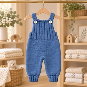 May include: A blue knitted overall featuring a ribbed chest panel, two white buttons at the shoulder straps, and ribbed cuffs at the ankles. The garment is constructed with a stockinette stitch on the legs and a vertical rib stitch on the bodice.