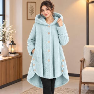 May include: A light blue hooded coat made of fuzzy, textured fleece material. The coat features a front button closure with five visible buttons and three additional decorative buttons on each side of the lower hemline.