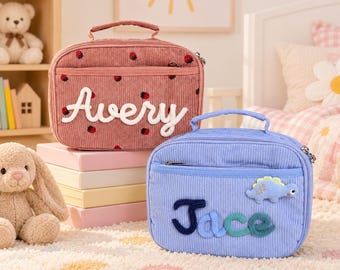 以下が含まれることがあります： イチゴ柄のピンクのコーデュロイ製ランチバッグには白でAveryと刺繍され、水色の恐竜のワッペンが付いた青いコーデュロイ製ランチバッグには濃い青と緑でJaceと刺繍されています。