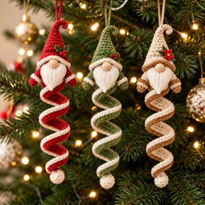 May include: Three crochet gnome ornaments hanging vertically. Each gnome features a pointed hat, a white yarn beard, and a long, spiraling body. The first is red, the second is green, and the third is beige, each with festive accents.