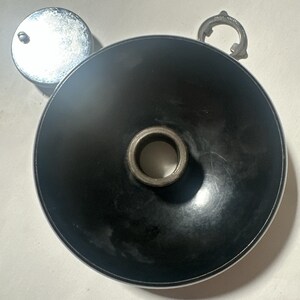 May include: A circular black component with a central metallic opening, accompanied by a separate small chrome-finished circular cap and a thin metallic ring component with a small tab, all presented as individual mechanical parts.