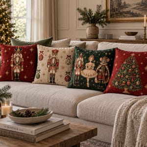 May include: Four square throw pillows featuring Christmas themes. One is red with a nutcracker, one is cream with a nutcracker and ornaments, one is dark green with a nutcracker, ballerina, and mouse king, and one is red with a decorated tree.