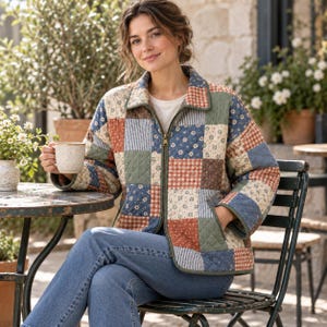 Woman sitting outdoors at a table wearing a handmade quilted patchwork jacket with long sleeves and front zip.⁠