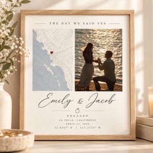 May include: A framed print titled THE DAY WE SAID YES featuring a map with a red heart, a photograph of a couple on a beach, the names Emily & Jacob, a ring icon, the word ENGAGED, the location La Jolla, California, and the date April 12, 2024.