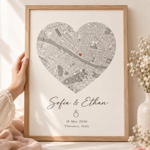 May include: A framed print featuring a heart-shaped map of Florence, Italy, with a small red heart marking a location. Below the map, the text reads Sofia & Ethan, followed by a ring icon, the date 18 May 2026, and the location Florence, Italy.