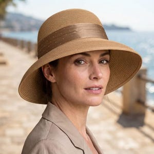 May include: A tan sun hat with a rounded crown and a wide, downward-sloping brim. The hat features a smooth, satin-like ribbon band in a slightly darker shade of tan, accented with a subtle pattern of tiny, evenly spaced metallic dots.