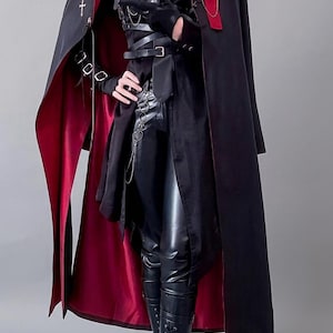 May include: A black long coat with a red lining, worn over a black shirt, tie, and leather-look trousers. The outfit includes a black chest harness with buckles, silver chain accents, a red rose lapel pin, and black lace-up boots with silver hardware.