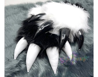 May include: A pair of black and white faux fur paw-shaped hand warmers with white claws. The claws are made of a shiny material.