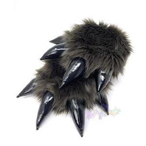 May include: A pair of brown furry paw slippers with black claws. The claws are made of a shiny material and are pointed.