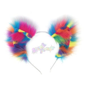 May include: Rainbow furry cat ears headband with a silver metal headband. The ears are made of a fluffy, multi-coloured fabric with a rainbow pattern.