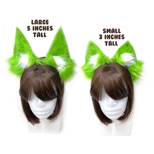May include: Two pairs of green and white faux fur cat ears, one pair is 5 inches tall and the other is 3 inches tall. The ears are on a headband and are worn by a mannequin with brown hair.