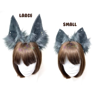 Op de afbeelding: Twee paar grijze wolvenoren, één paar met het label "LARGE" en het andere met het label "SMALL", worden getoond op twee verschillende modellen met bruin haar. De oren zijn gemaakt van zacht, pluche bont en hebben een hoofdband.