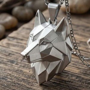 May include: A silver-toned metal pendant shaped like a geometric wolf head, featuring sharp, angular facets and a brushed finish. The pendant is suspended from a matching silver-toned metal chain with elongated oval links, creating a cohesive look.