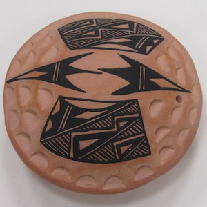 Puede incluir: Un plato redondo de cerámica de color terracota con diseños geométricos negros. El plato tiene un borde elevado con un borde festoneado.