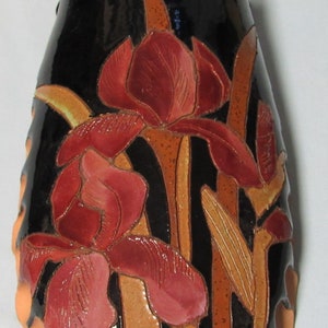 May include: A black ceramic vase with a raised design of red and brown irises. The vase has a scalloped edge.