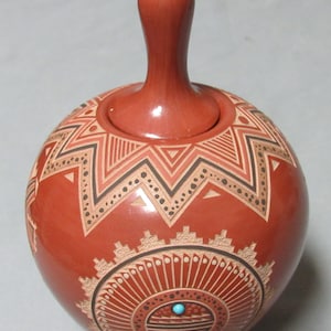May include: A red clay pottery jar with a geometric design and a turquoise stone accent. The jar has a lid with a knob on top.