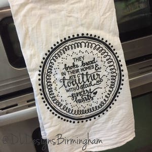 May include: A white kitchen towel with a black circle design. The circle contains the text "THEY broke bread IN THEIR HOMES & ATE together WITH glad AND sincere hearts".