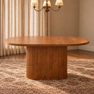 Puede incluir: Una mesa de comedor ovalada grande hecha de madera de tono medio. La mesa presenta una superficie lisa y plana, sostenida por una base de pedestal única y sustancial caracterizada por una textura vertical acanalada o estriada en todo su exterior.