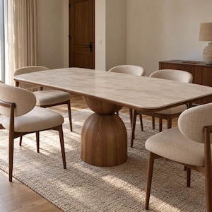 Peut inclure: Une table à manger rectangulaire avec un plateau aspect pierre beige clair et un pied central en bois foncé, entourée de quatre chaises dotées de structures en bois foncé et d'assises et dossiers incurvés en tissu beige clair.