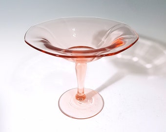 May include: A pink glass pedestal bowl with a fluted rim and a delicate stem. The bowl is perfect for serving desserts or snacks.