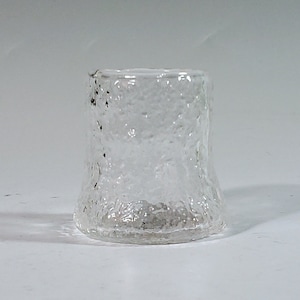 May include: A clear glass tumbler with a textured, frosted surface. The glass has a wide base and a slightly flared rim.