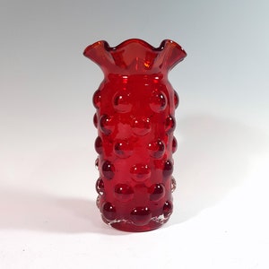 May include: A red glass bud vase with a ruffled top and a textured, bubbled surface.