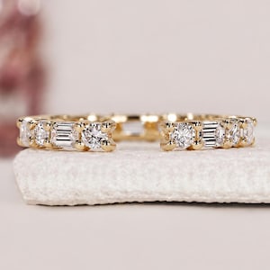 May include: A gold open-style ring featuring an alternating pattern of round brilliant-cut stones and rectangular baguette-cut stones set along the band. The ring has a polished gold finish and is open at the front, showcasing clear, faceted stones.