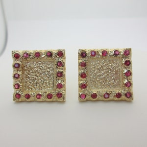 May include: A pair of gold square earrings with a textured surface and a border of small pink gemstones.