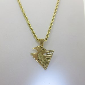 Puede incluir: Un collar de cadena de oro con un colgante en forma de tri&aacute;ngulo con un dise&ntilde;o de p&aacute;jaro. El colgante tiene una superficie texturizada.
