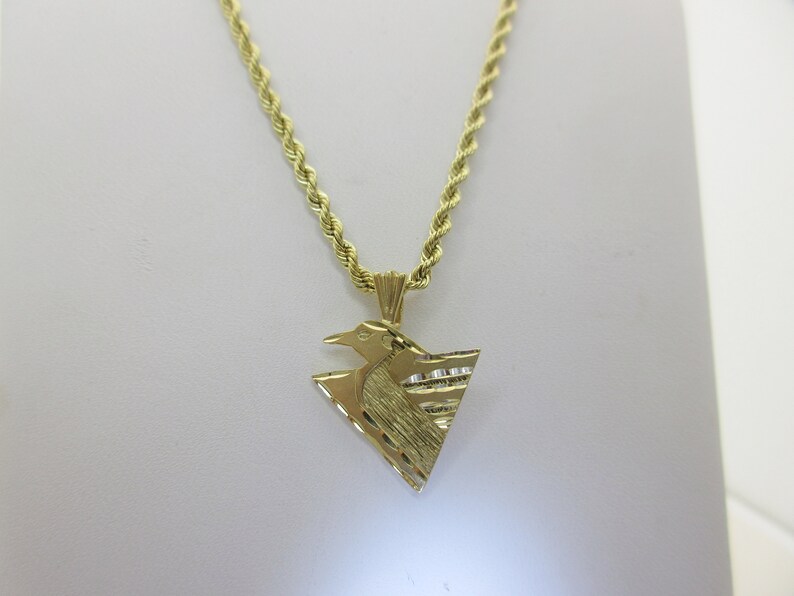 Puede incluir: Un collar de cadena de oro con un colgante en forma de tri&aacute;ngulo con un dise&ntilde;o de p&aacute;jaro. El colgante tiene una superficie texturizada.