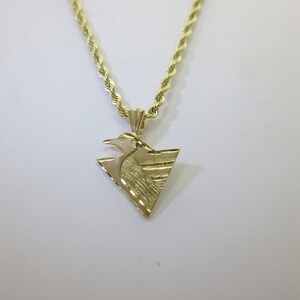 Puede incluir: Un collar de cadena de oro con un colgante que presenta un dise&ntilde;o de p&aacute;jaro estilizado en forma triangular.