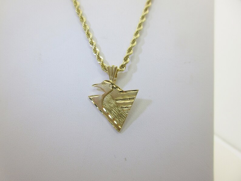 Puede incluir: Un collar de cadena de oro con un colgante que presenta un dise&ntilde;o de p&aacute;jaro estilizado en forma triangular.