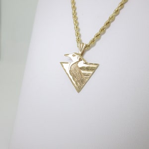 Puede incluir: Un collar de cadena de oro con un colgante triangular que presenta un dise&ntilde;o de p&aacute;jaro estilizado.