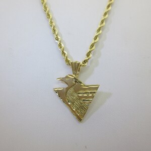 Puede incluir: Un collar de cadena de oro con un colgante que presenta un dise&ntilde;o de p&aacute;jaro estilizado. El colgante tiene forma de tri&aacute;ngulo con una superficie texturizada.