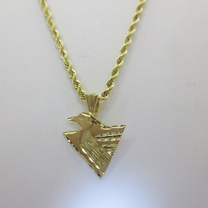 Puede incluir: Un collar de cadena de oro con un colgante que presenta un dise&ntilde;o de p&aacute;jaro estilizado. El colgante tiene forma triangular y una superficie texturizada.