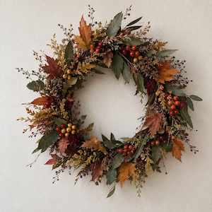 May include: A circular wreath constructed from a woven twig base, adorned with a mix of dried autumn foliage including maple leaves in shades of orange, red, and brown, interspersed with green bay leaves, yellow sprigs, and clusters of red and yellow berries.