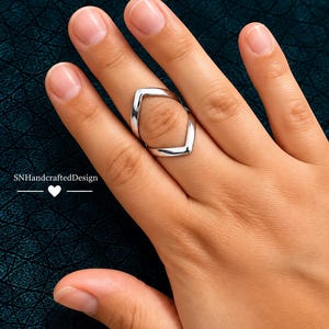 May include: A silver-toned ring featuring a double chevron design that creates an open, diamond-shaped gap in the center. The band is smooth and polished, wrapping around the finger with two pointed V-shaped sections facing each other.