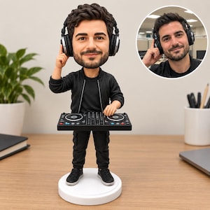 Pode incluir: Uma estatueta bobblehead personalizada de uma pessoa com cabelo escuro e barba, vestindo jaqueta e calças pretas, sobre uma base circular branca. A figura usa fones de ouvido pretos e opera um controlador de DJ preto com botões coloridos.